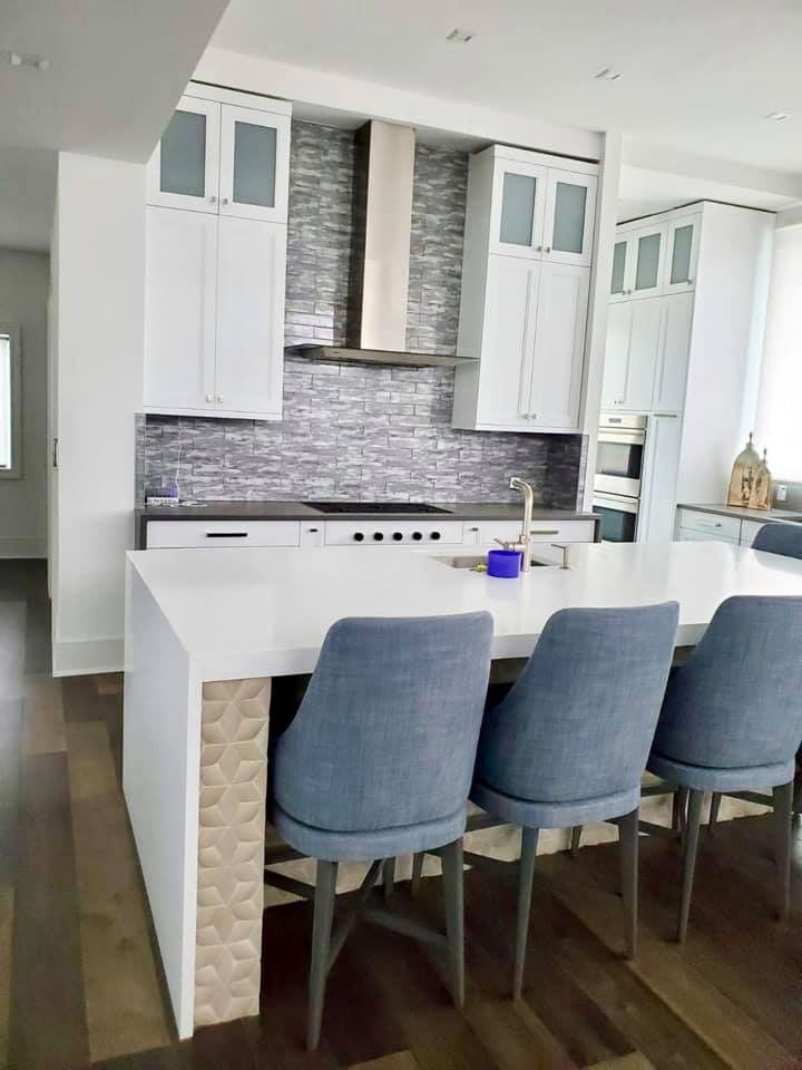 Modern white kitchen island with gray bar stools, white cabinets, and a mosaic tile backsplash