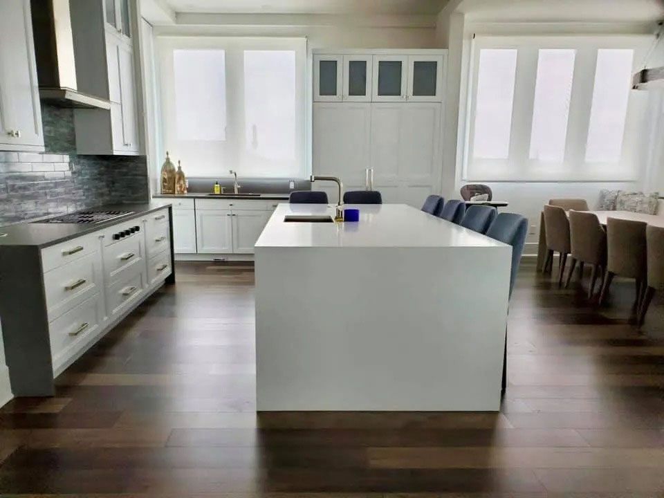 Bright modern kitchen with white island, cabinets, dark floor, and dining chairs by the windows