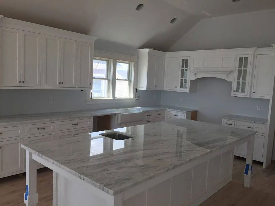 Bright white kitchen with marble island, cabinets, and windows, under renovation with plastic-covered fixtures
