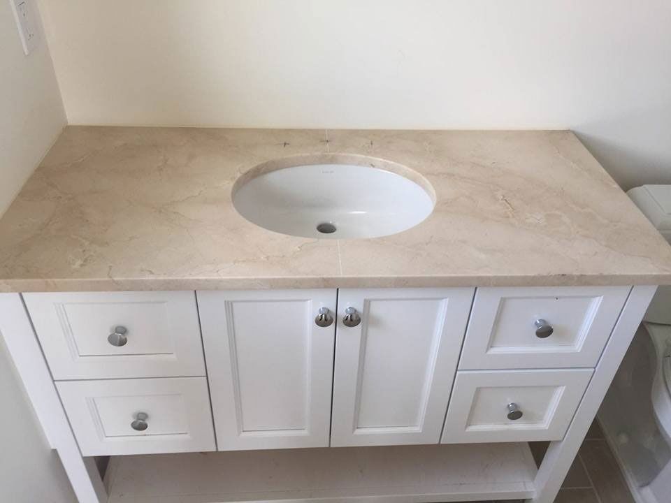 White bathroom vanity with beige countertop and round sink cutout against a plain wall