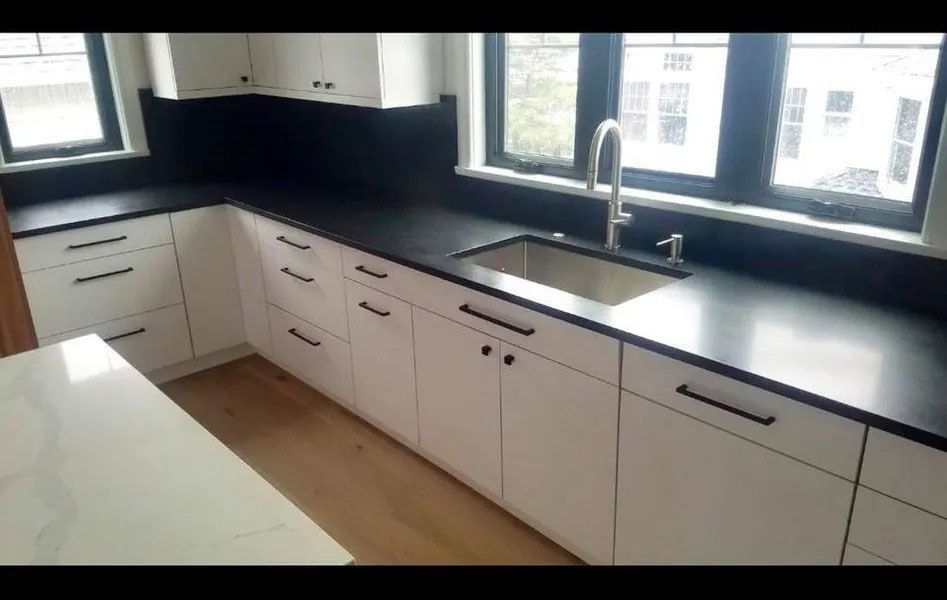 Modern kitchen with black countertops, white cabinets, sink, and large windows