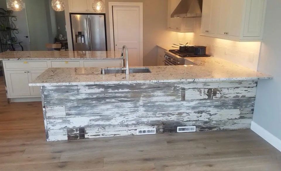 Modern kitchen with a large distressed white island, marble countertops, stainless fridge, and light wood floor