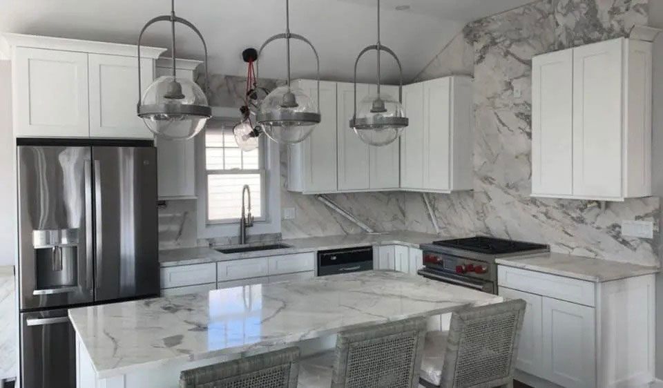 Modern white kitchen with marble countertops, stainless steel appliances, and glass pendant lights.
