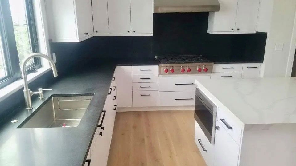 Bright modern kitchen with white cabinets, black backsplash, wood floor, and a large island.