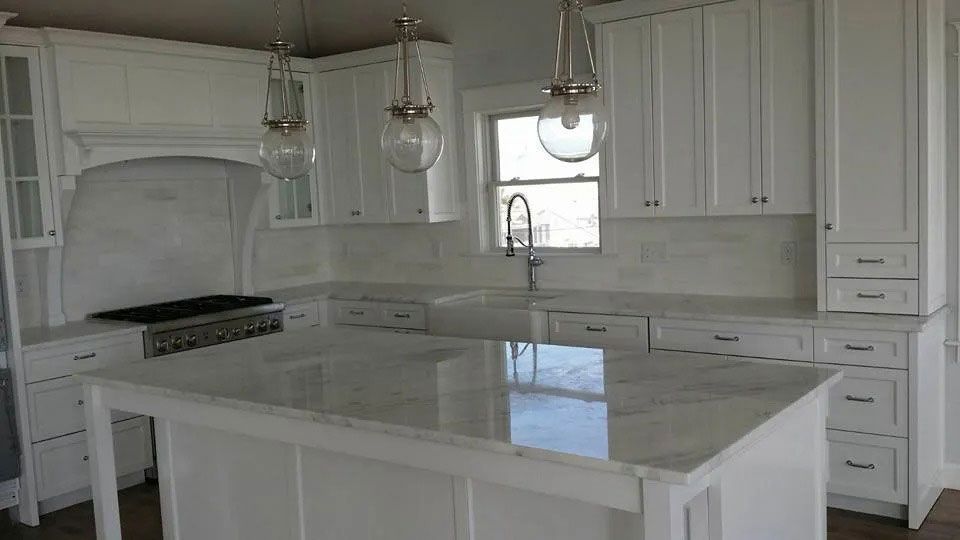 Bright white modern kitchen with a large island, pendant lights, and a range hood