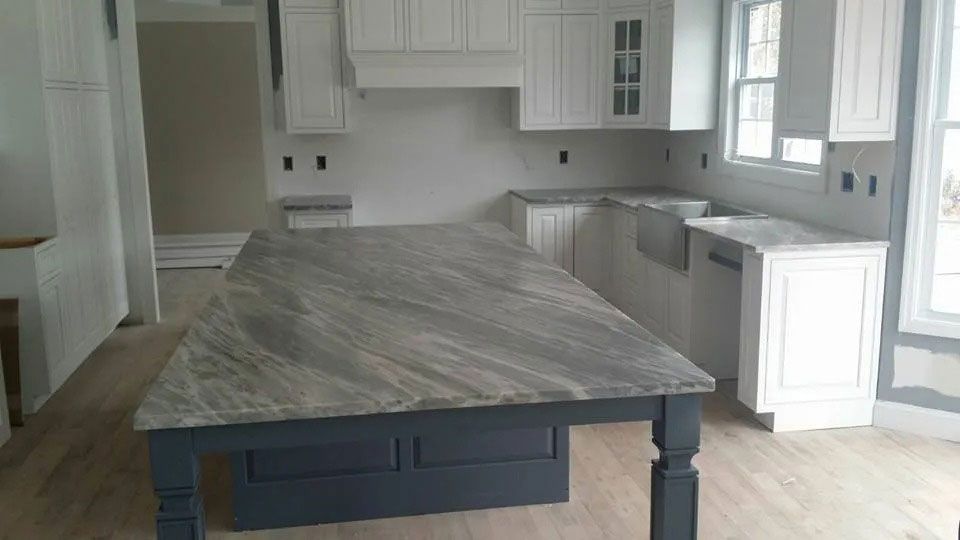 Bright white kitchen with gray cabinets and a large dark island countertop in the foreground