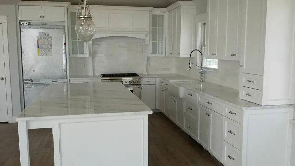 Bright white modern kitchen with island, cabinets, stainless fridge, and gas stove