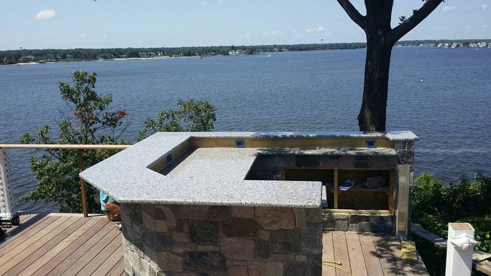 Stone outdoor grill beside a wooden deck overlooking a calm lake and distant shoreline