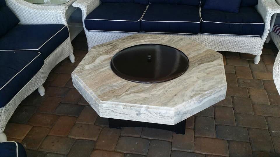 Octagonal stone fire pit with dark bowl, surrounded by blue-and-white outdoor seating on brick patio