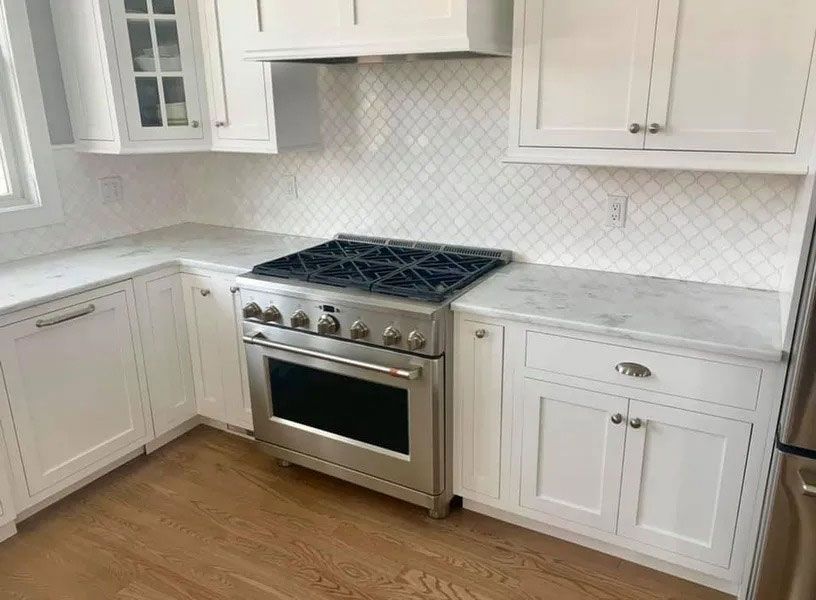 White kitchen with stainless steel stove, white cabinets, and marble-look countertops.