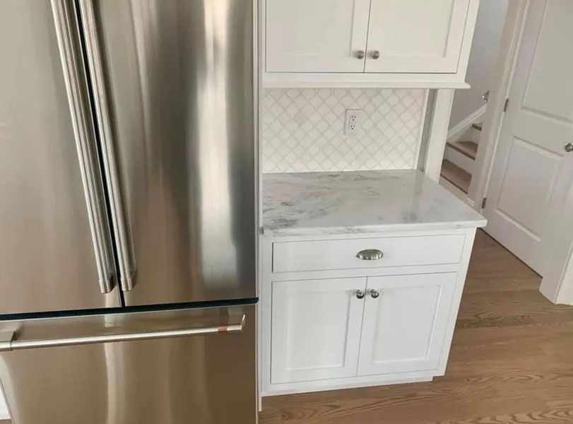 Stainless steel refrigerator beside a white kitchen cabinet and countertop in a bright kitchen