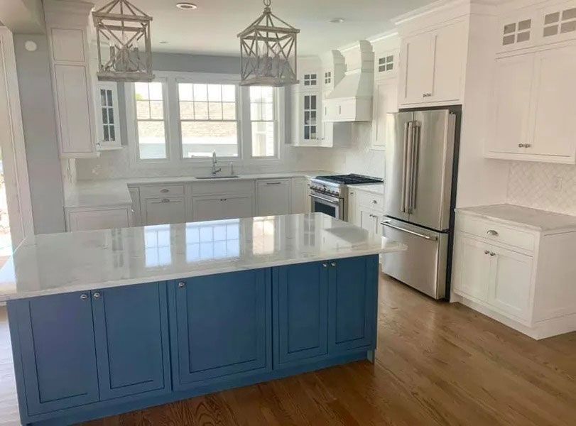 Bright kitchen with blue island, white cabinets, stainless fridge, and large windows