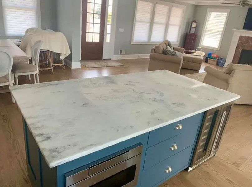Kitchen island with white marble top and blue cabinetry in a bright open living room