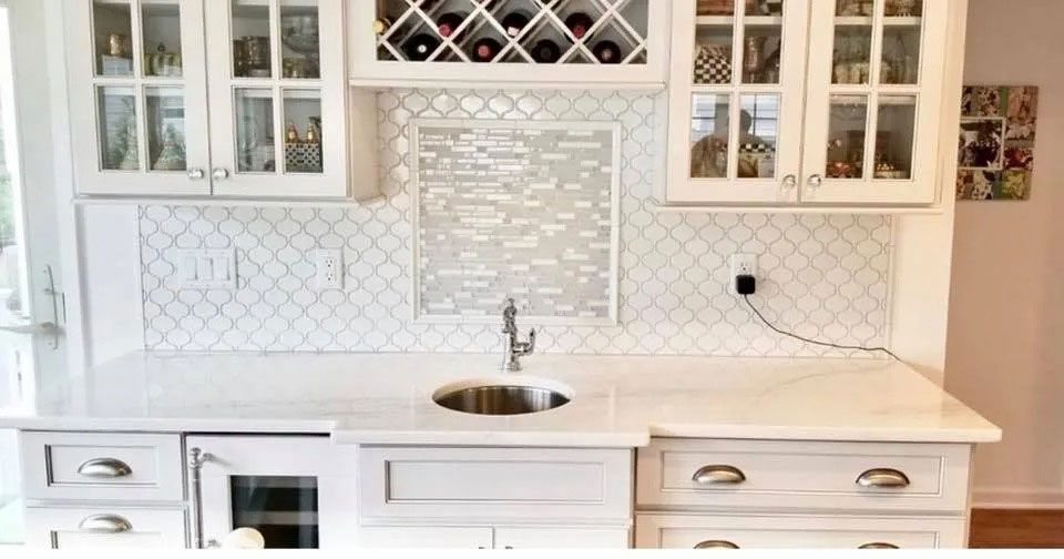 White kitchen with marble countertops, sink, cabinets, and built-in wine racks behind the sink