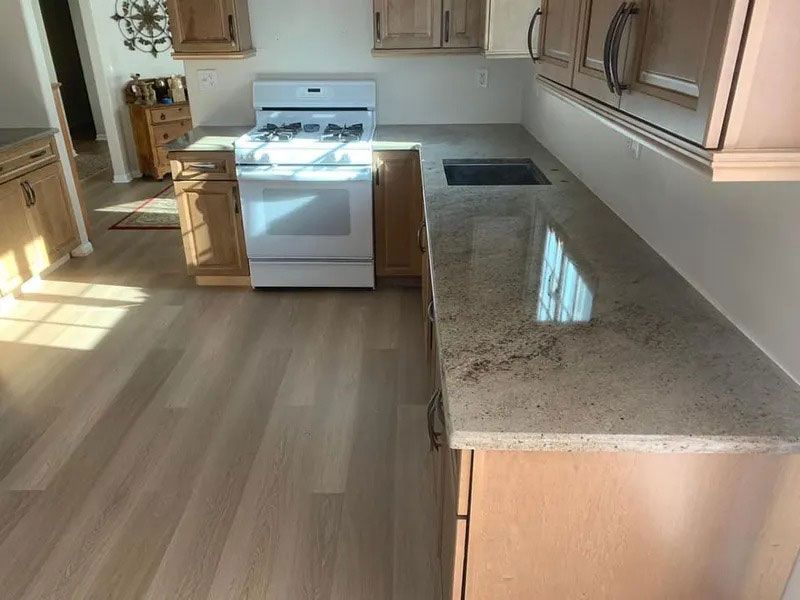 Empty kitchen with white stove, wood cabinets, and granite countertop lit by sunlight.