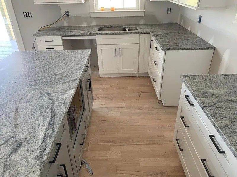 Empty kitchen with gray granite countertops, white cabinets, and light wood floors