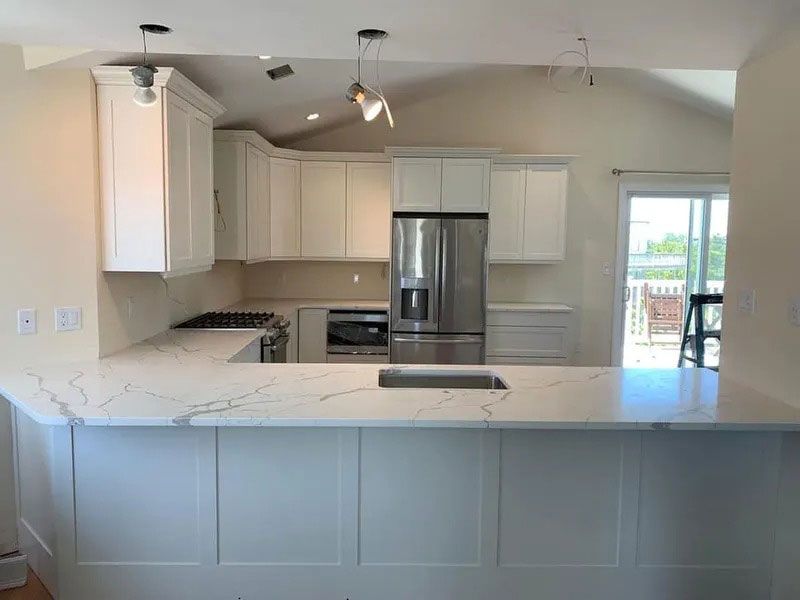 Bright modern kitchen with white cabinets, stainless steel fridge, and large marble island.