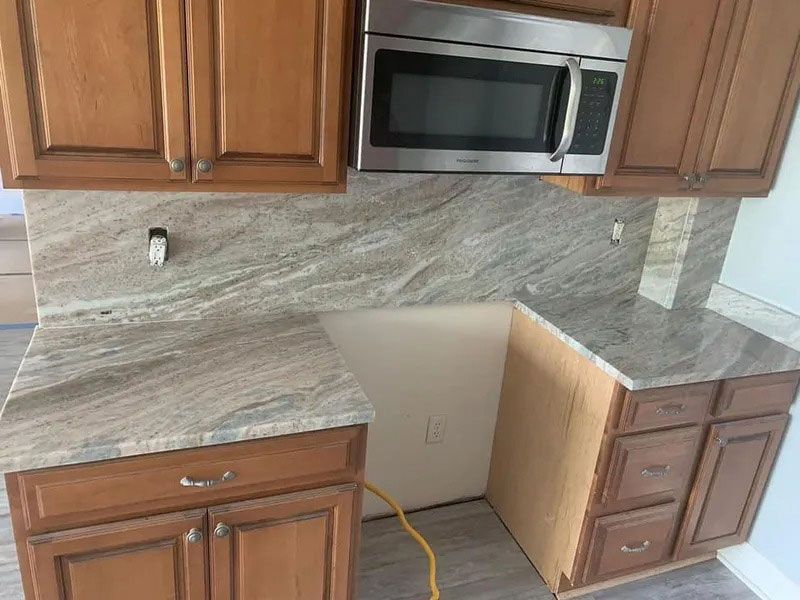 Kitchen counter with cabinets, a microwave, and a partially installed wooden cabinet under the countertop.