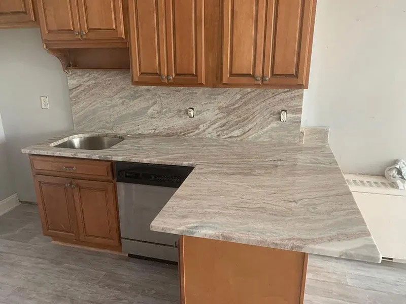 Small kitchen with wood cabinets, stainless sink, black dishwasher, and light stone countertop.