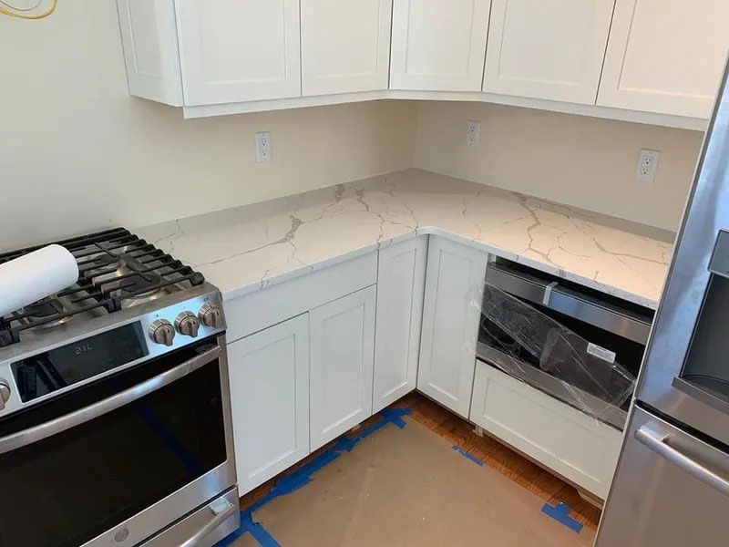 Modern white kitchen corner with white cabinets, marble-look counters, stainless oven, and built-in dishwasher.