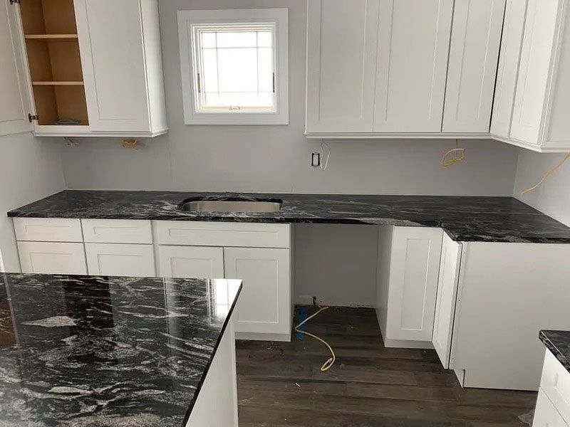 Partially finished kitchen with white cabinets, dark marble countertops, and exposed flooring under the sink area