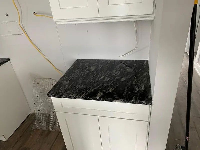 White laundry cabinet with black marble top in a small utility room, with wall cabinets above.
