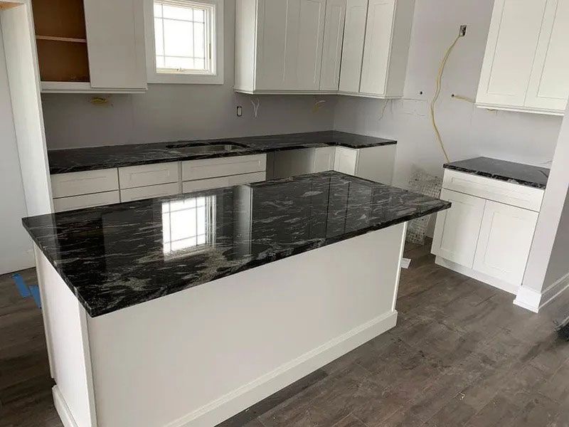 Empty kitchen with white cabinets, gray flooring, and black marble island countertop
