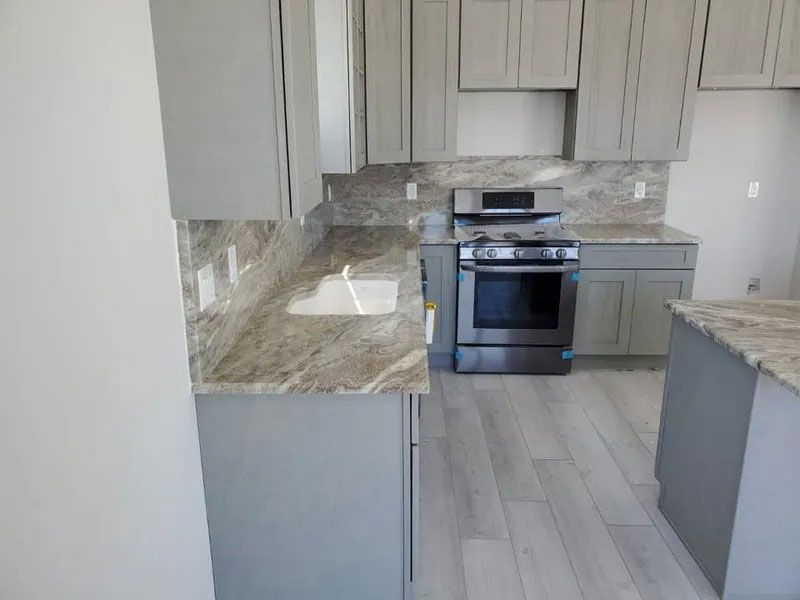 Modern kitchen with gray cabinets, marble countertops, and stainless steel stove on light wood flooring