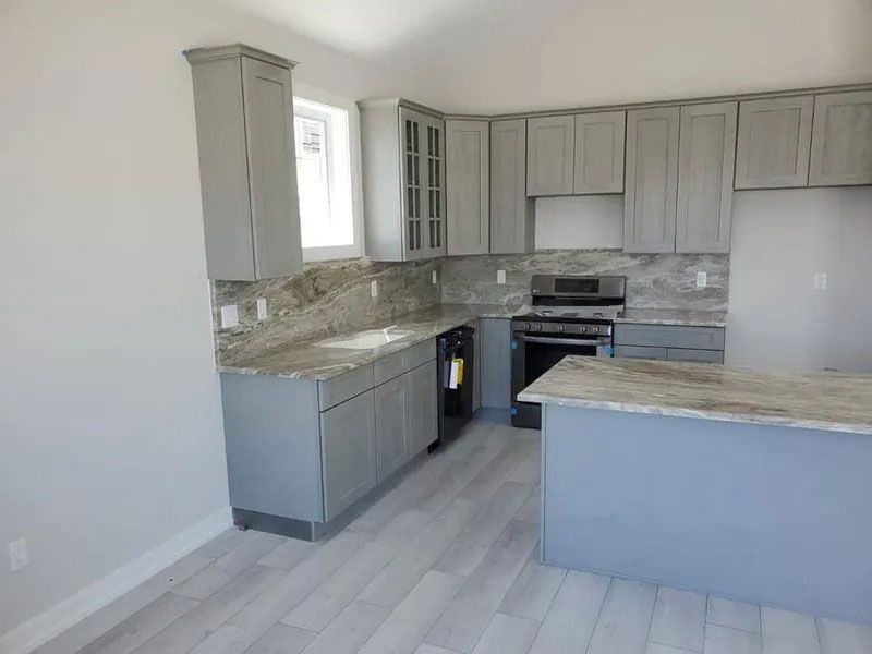 Empty modern kitchen with light gray cabinets, marble countertops, and a peninsula island.