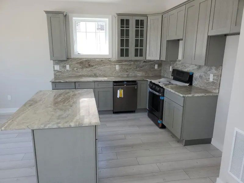 Modern kitchen with gray cabinets, marble island, stainless appliances, and light wood flooring