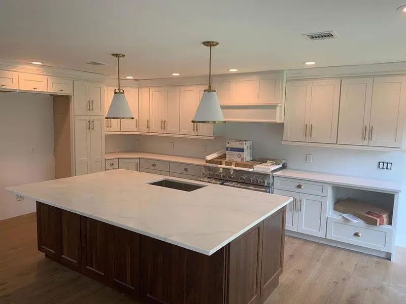 Modern white kitchen with central island, pendant lights, and unfinished cabinets and appliances along the back wall
