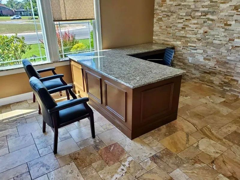 Modern office with stone tile floor, granite desk, two black chairs, and large window with outdoor view