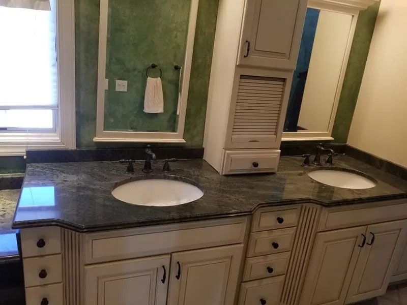 Double vanity bathroom with white sinks, dark countertop, beige cabinets, and green walls with mirrors.