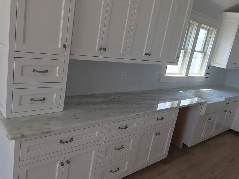 White kitchen cabinets with marble-look countertops and a window above the sink.