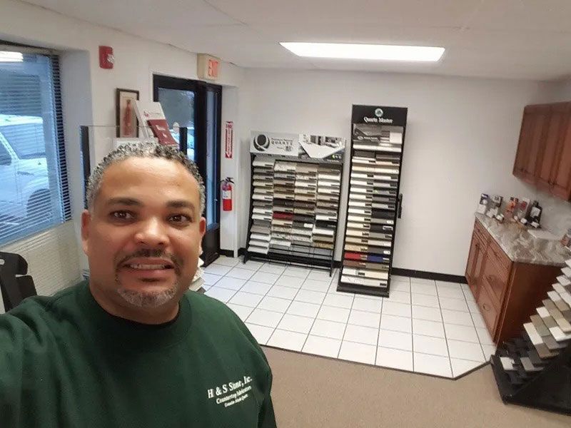 Man taking a selfie in a tiled office or salon with shelving and product displays in the background