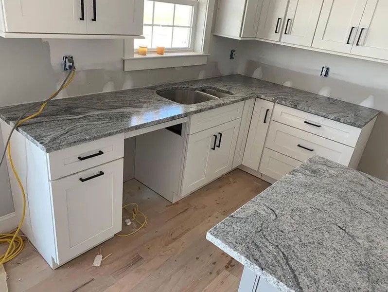 L-shaped kitchen with white cabinets and granite countertops under installation, with tools and a bare cabinet opening.