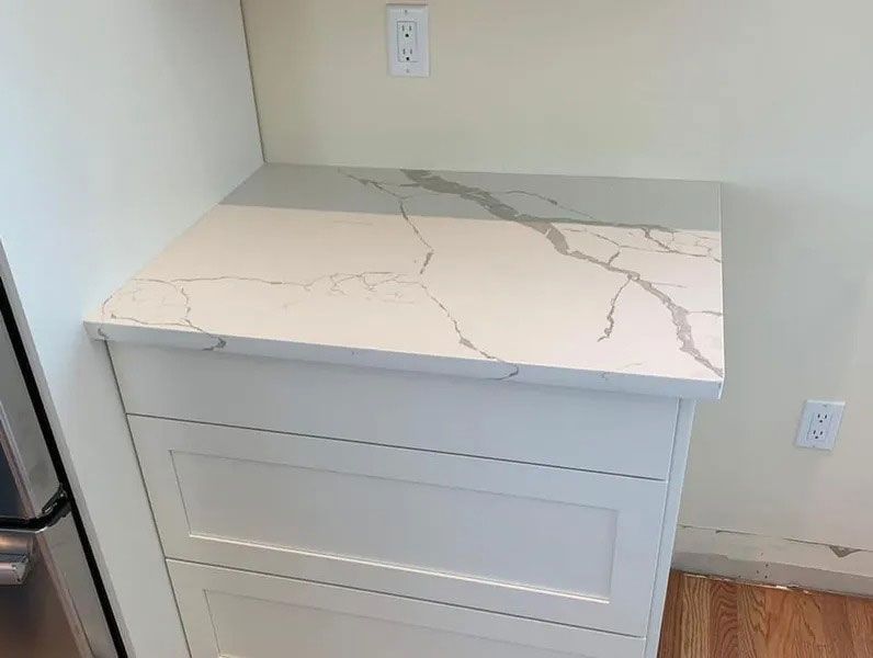 White cabinet with a marble-look countertop against a beige wall, near an outlet.