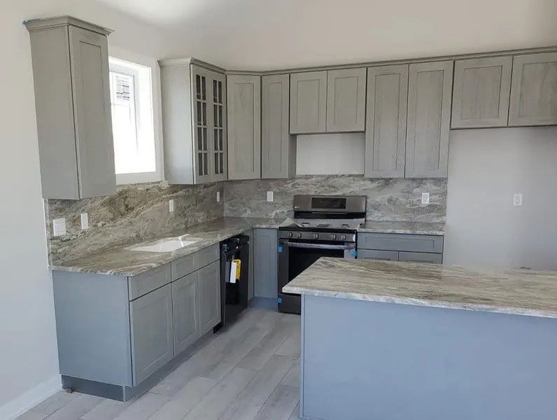 Empty modern kitchen with white cabinets, gray countertops, stainless stove, and tiled backsplash