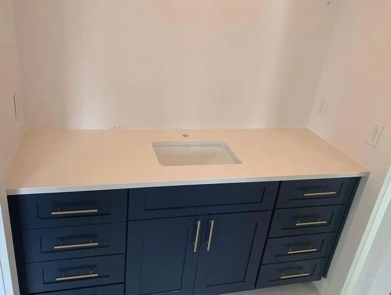 Blue vanity cabinet with drawers and double doors beneath a beige countertop with a sink cutout