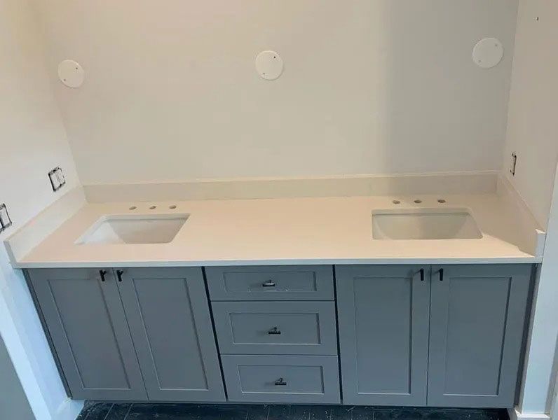 Built-in bathroom vanity with light countertop, two sinks, and blue-gray cabinets against a white wall