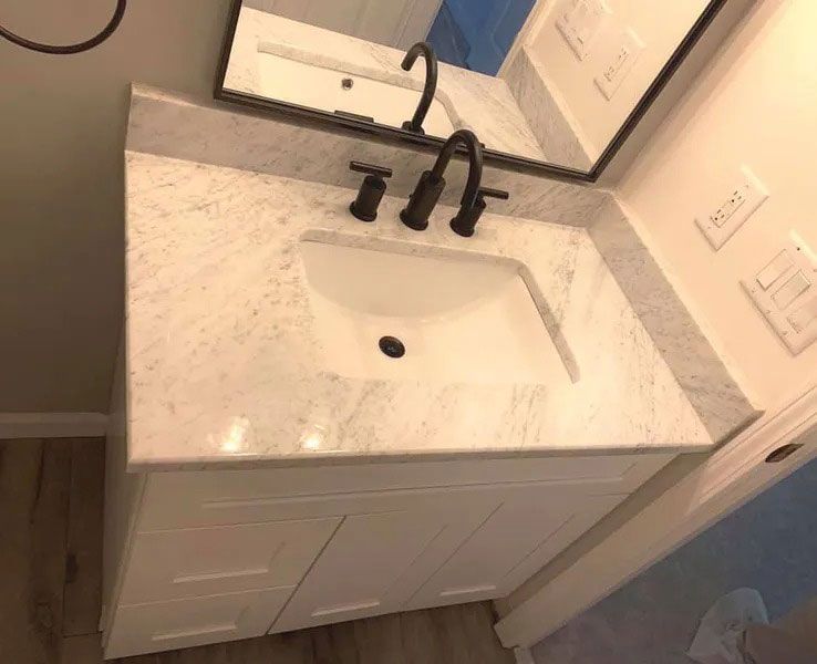 White bathroom vanity with black faucet and rectangular sink under a mirror.