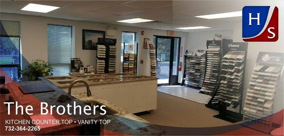 Modern kitchen showroom with cabinets, island, and display racks; The Brothers logo in corner