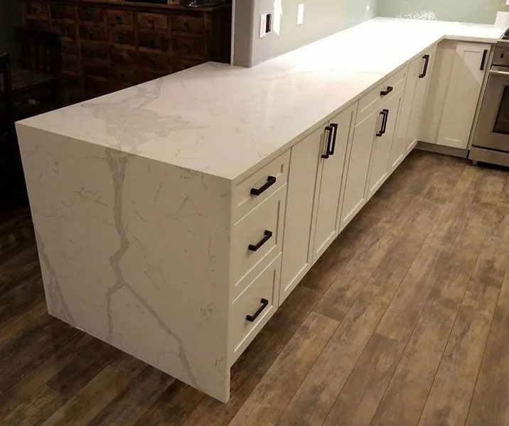 White quartz kitchen island with drawers and black handles on a wood floor
