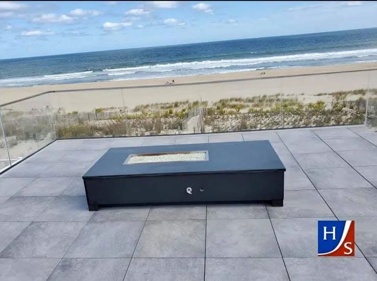 Low black bench on a tiled patio overlooking a sandy beach and ocean