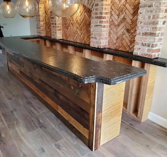 Long rustic wood bar with black countertop in a brick-walled room