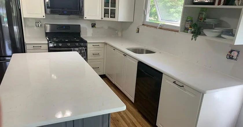 Bright white kitchen with island, white cabinets, black stove, and sink beneath a window