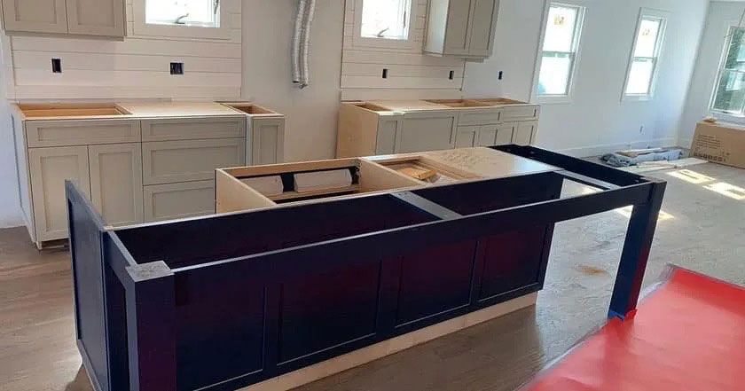 Empty kitchen under renovation with dark cabinets, white walls, and a red floor covering