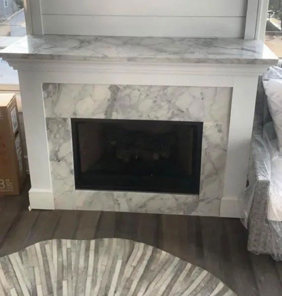 White marble fireplace with black firebox in a living room, shown with part of a round rug on the floor