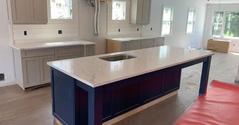 Modern kitchen with white cabinets, central island, and bright windows; red protective floor covering visible