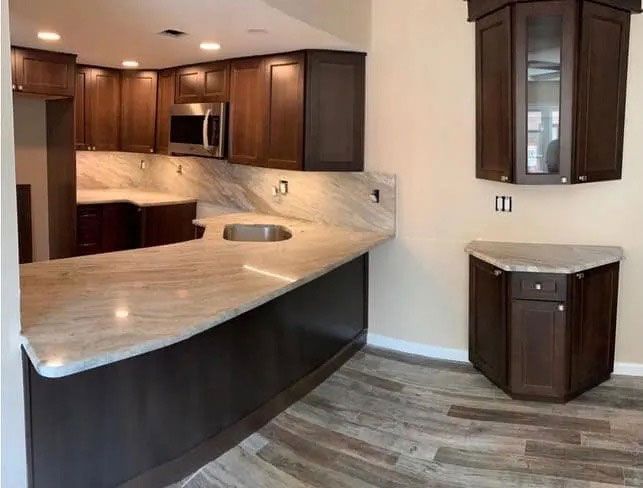 Modern kitchen with dark wood cabinets, light countertops, and a small corner cabinet on a wood-look floor